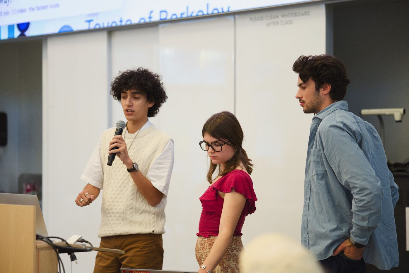 Three builders present their project with a microphone at the front of the room